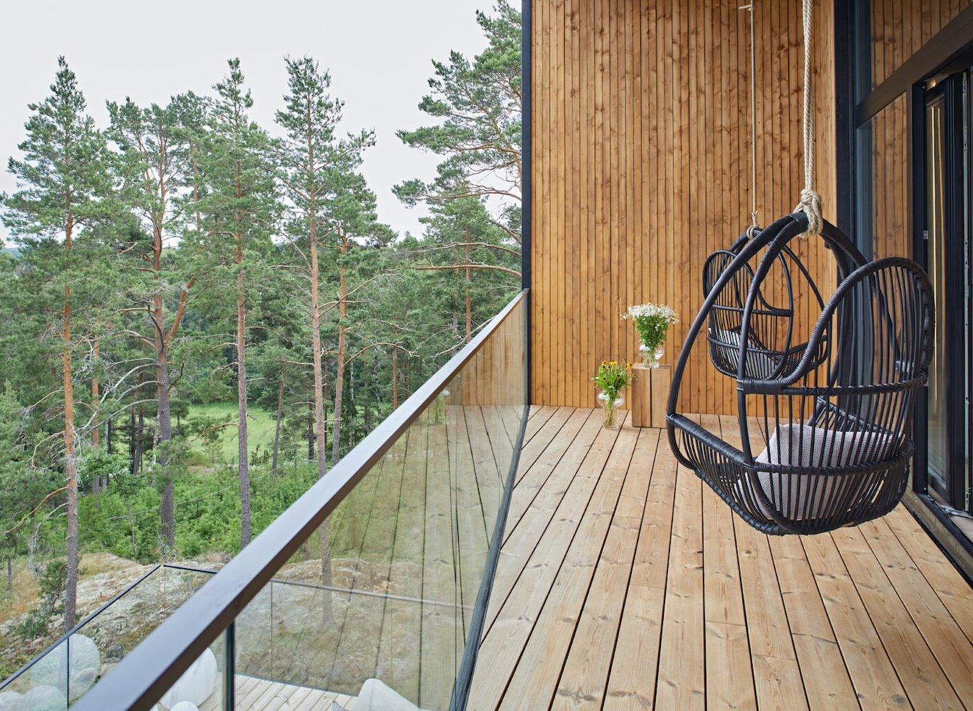 Modern wooden deck with hanging chair overlooking forest and hills with metal railings